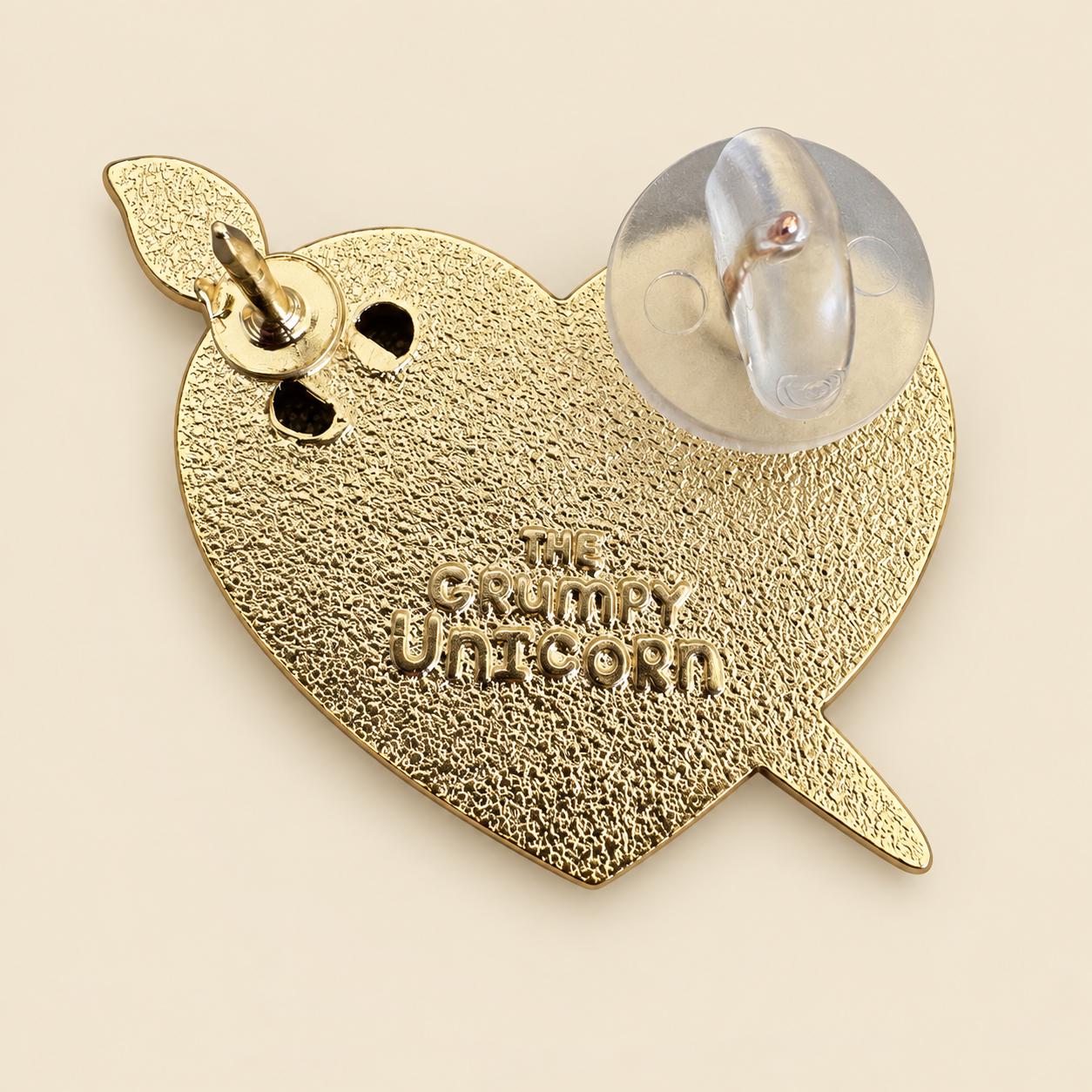 Back of the Art Heart enamel pin, gold plating stamped The Grumpy Unicorn with two pin posts and a rubber clutch