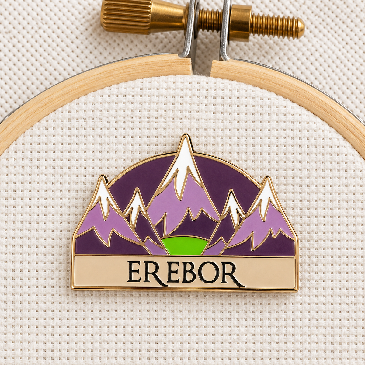Erebor Needle Minder on an embroidery hoop, purple mountain enamel needle minder with an Erebor banner and gold finish