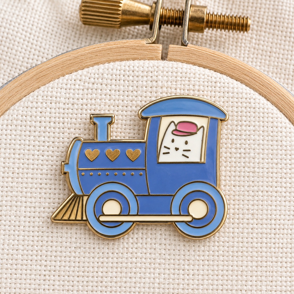 Cat Train Frank Needle Minder on an embroidery hoop, white cat driving a blue steam train