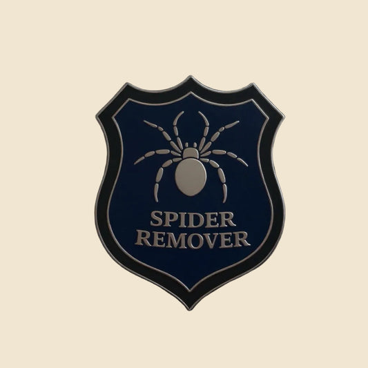Spider remover second-grade enamel pin on a cream background