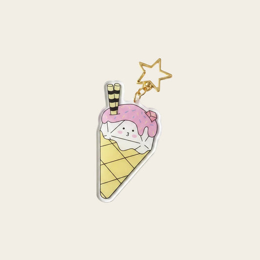 Dice Cream Charm — clear acrylic charm in the shape of a d20 ice cream cone (single scoop with pink frosting drizzle, sprinkles, gold star keyring), photographed on a pastel colour-blocked surface next to a real ice cream cone for scale. D&D dice charm.