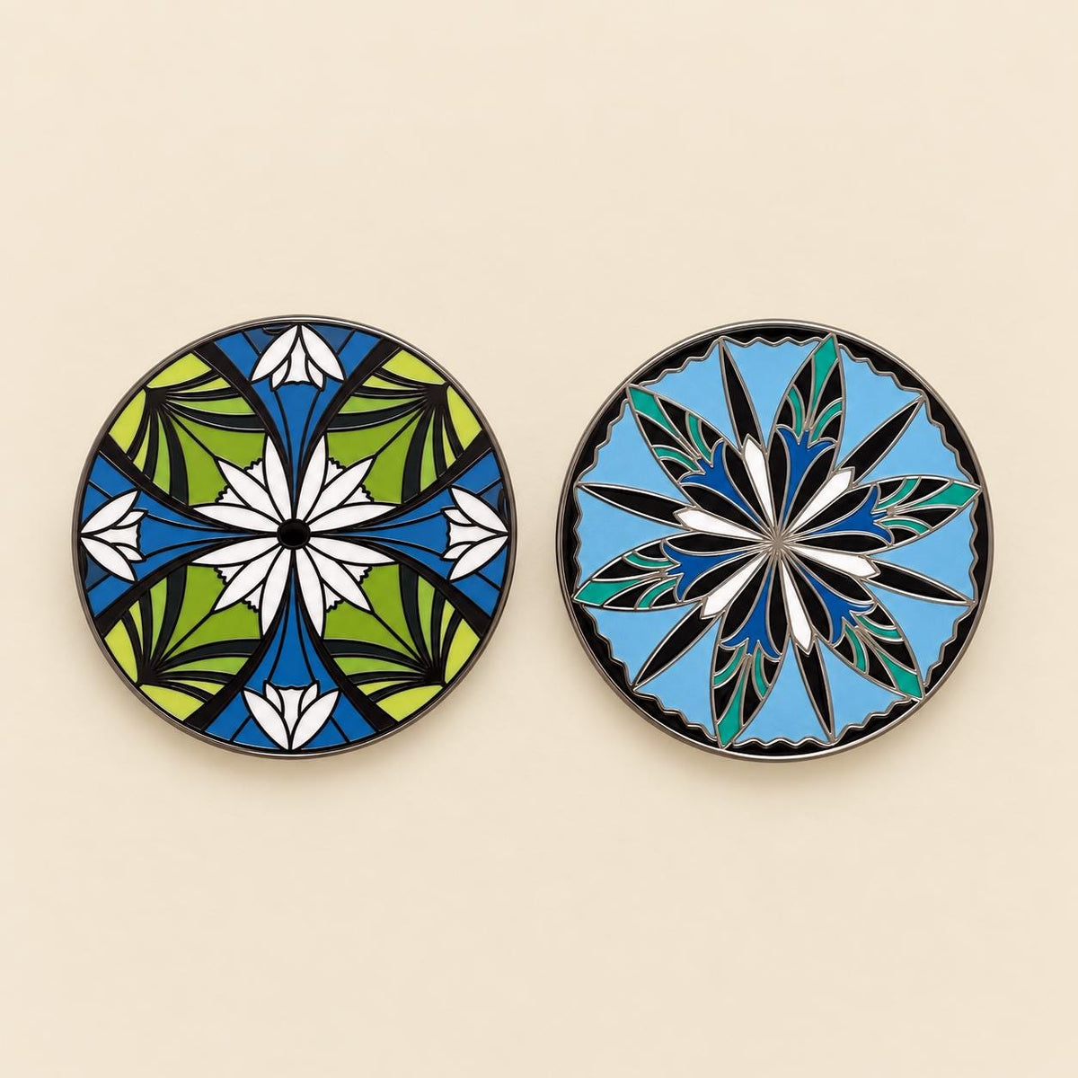 Two round elven flower enamel pins side by side, one green with white flowers, one sky blue with a twelve point star