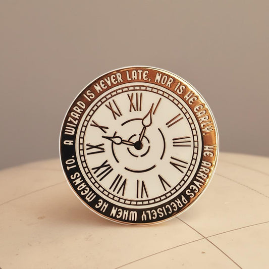 A Wizard is Never Late pin — round clock face with Roman numerals and the Gandalf quote etched around the rim, on a cream surface