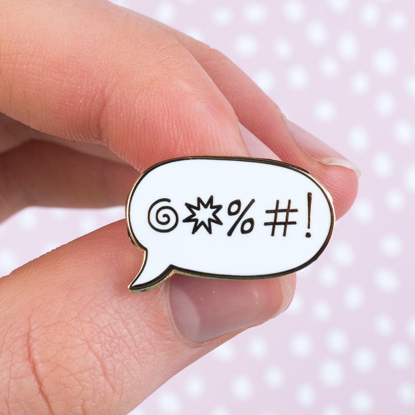White sweary speech-bubble enamel pin held in fingers for scale, funny lapel pin