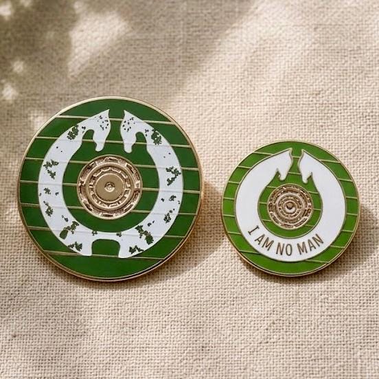 Size comparison: Shieldmaiden's Shield pin beside the smaller Éowyn's Shield I Am No Man pin