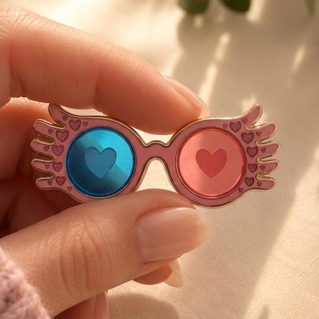 Moonstruck winged heart glasses enamel pin, gold with blue and pink transparent heart lenses