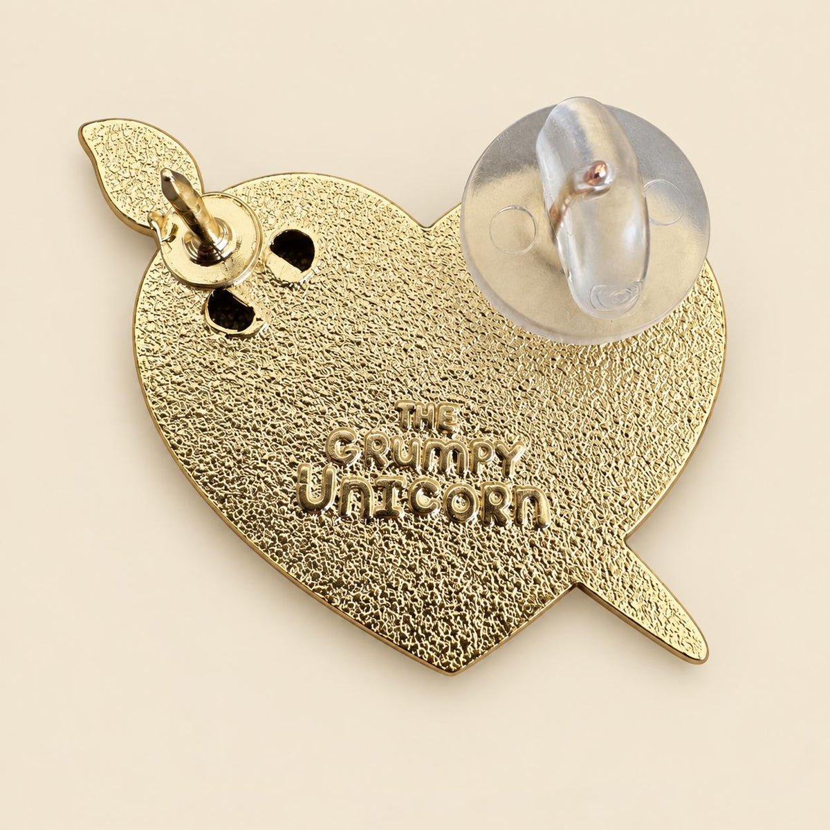 Back of the Art Heart enamel pin, gold plating stamped The Grumpy Unicorn with two pin posts and a rubber clutch