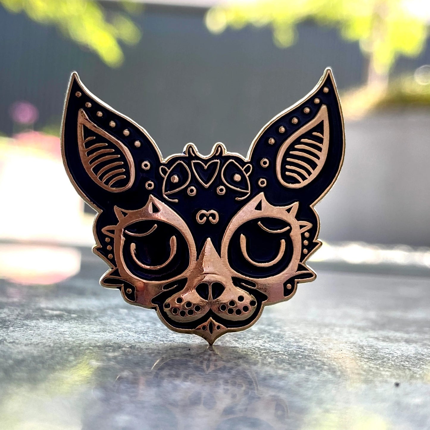 3D Jackal pin — ornate copper jackal face with Egyptian-style decorative patterns, on a stone surface with green bokeh