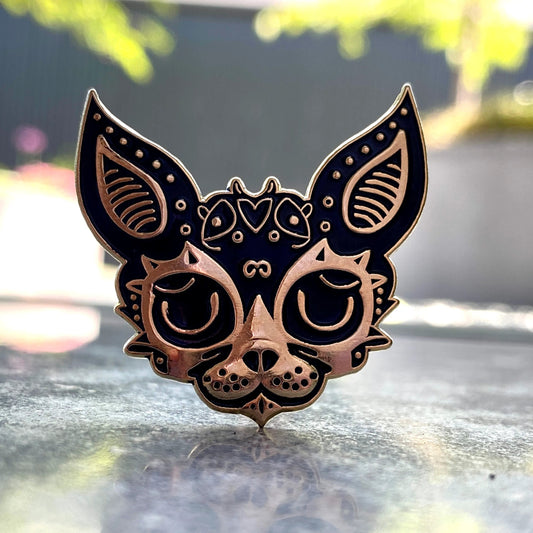 3D Jackal pin — ornate copper jackal face with Egyptian-style decorative patterns, on a stone surface with green bokeh