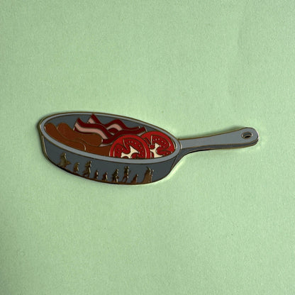 Sam's Saucepan pin on green - frying pan with bacon, sausages and tomato slices, Fellowship silhouettes on the side, LOTR enamel pin